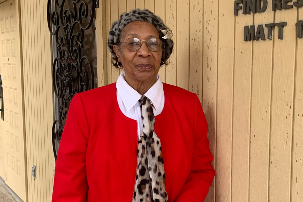 Ethel Baker, an older Black woman wearing a red shirt, stands outside St. Augustine Church in North Little Rock.