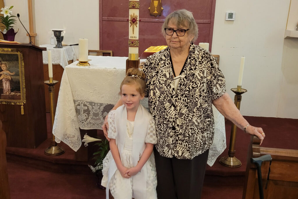 Marietta Marcotte, an older white woman in a leopard print shirt, stands beside her granddaughter, who is wearing a white dress, in front of the altar at St. Leo in Hartford. 