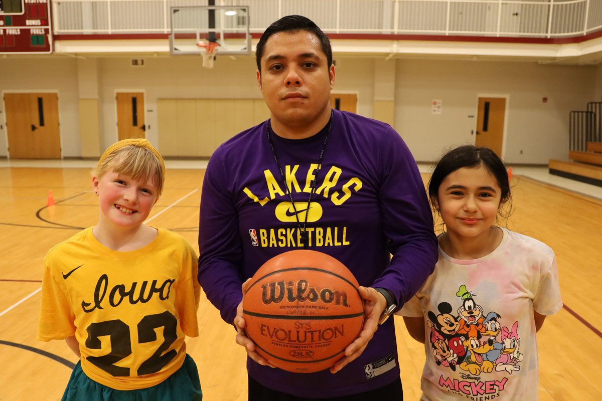 From left to right, a young white, a young Hispanic man, and a young Hispanic girl stand in the gymnasium at St. Theresa School in Little Rock.