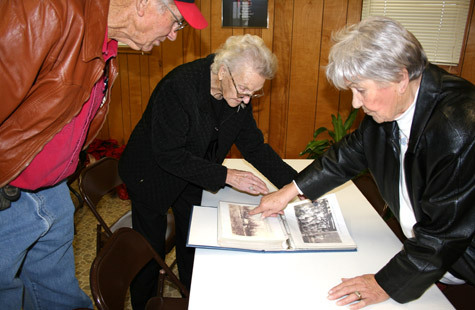 Agnes Ball (right) shows B.J.Breckenridge (left) a photo of a priest in a mule-drawn wagon on his way to celebrate Mass at the home of Elizabeth Coley (center) in the 1920s.