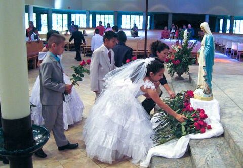 Children at their First Communion Mass at St. Vincent de Paul Church in Rogers present red roses in front of a statue of Mary May 19, 2012. Hispanic families often turn to the church for community and support.