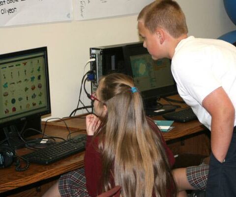 Student Brett Dineen, 12, helps out fellow advanced coder Olivia Chambers, 12, with a question in the Christ the King Coding Club. Students learn how coding relates to the world through fun computer projects.