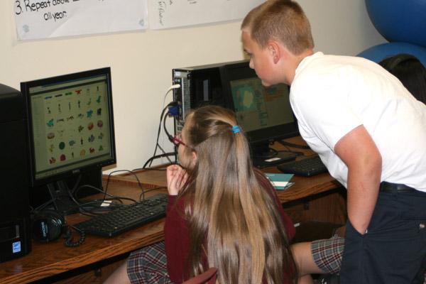 Student Brett Dineen, 12, helps out fellow advanced coder Olivia Chambers, 12, with a question in the Christ the King Coding Club. Students learn how coding relates to the world through fun computer projects.
