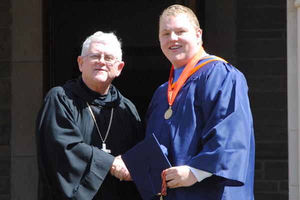 Jarrod Brown receives his diploma May 14 from Abbot Leonard Wangler during graduation at Subiaco Academy. Brown overcame several surgeries to repair a birth defect during his senior year at the school.