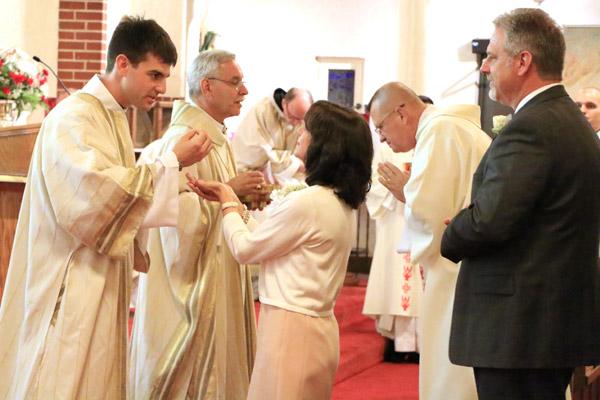 Deacon Mike Johns provides Communion to his mother, Julie, as his father, Michael, watches May 24 during his ordination to the transitional diaconate at Blessed Sacrament Church in Jonesboro.