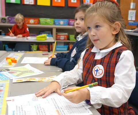Charlotte Hylden (right) and Anna Kiehn, first-grade students at Our Lady of the Holy Souls School in Little Rock, pay attention to teacher Amy Bratcher during a math lesson. The students both earned H.E.A.R.T. stickers.