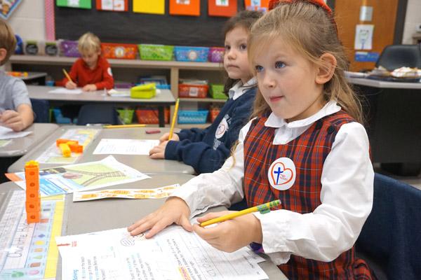 Charlotte Hylden (right) and Anna Kiehn, first-grade students at Our Lady of the Holy Souls School in Little Rock, pay attention to teacher Amy Bratcher during a math lesson. The students both earned H.E.A.R.T. stickers.