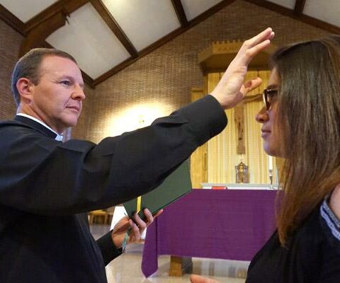 Father Erik Pohlmeier, diocesan director of faith formation, demonstrates the blessing that takes place during anointing of the sick with Jasmine Moore, secretary in the office of faith formation, at St. John Center in Little Rock.