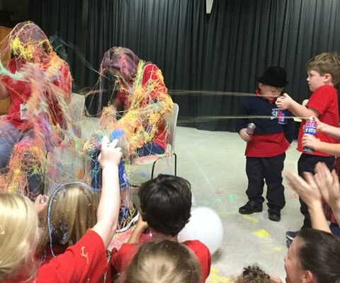 Our Lady of the Holy Souls students cover principal Nancy Handloser and vice principal Amber Bagby in silly string (photo at right) for surpassing their Raise Craze goal Oct. 19 during a school-wide assembly.