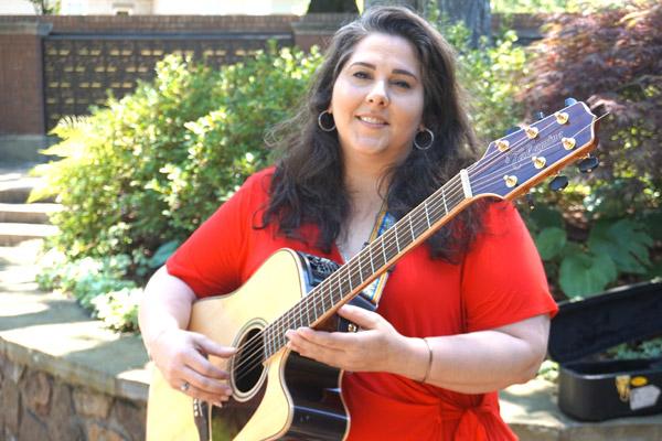 Susej Thompson, the pastoral music director at Our Lady of the Holy Souls in Little Rock, strums her guitar in the church courtyard June 19.