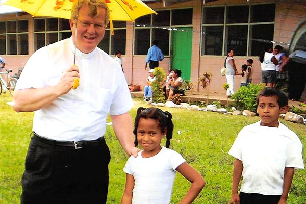 Bishop-elect Francis I. Malone smiles with children in front of Robert Noble School in La Colonia, Honduras, during a mission trip with Christ the King Church in 2005. As pastor, he has supported mission work and continued the tradition of a tithing parish.
