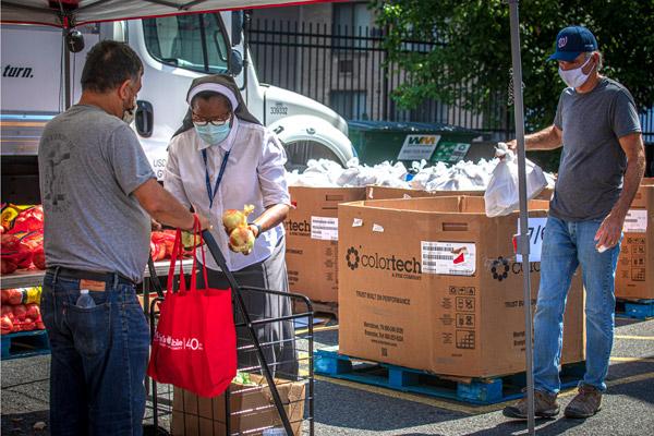 Sister Romana Uzodimma, a Sister of the Handmaids of the Holy Child Jesus, places onions into a man's bag at Catholic Charities' Spanish Catholic Center parking lot in Washington where he is picking up free food supplies July 15  during the pandemic. "No one should face hunger in a land of plenty," says the bishops' quadrennial "Faithful Citizenship" document.