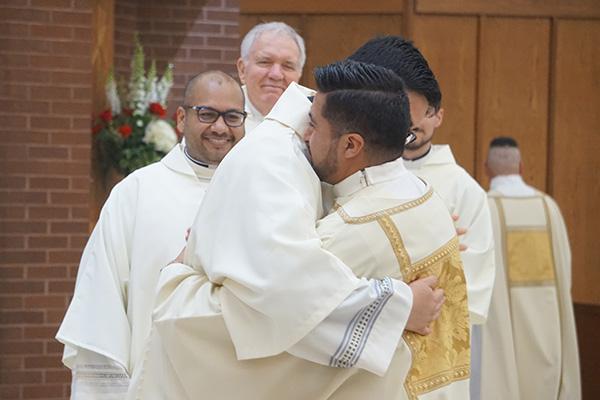 Close friend Deacon Omar Galv&aacute;n, who will be ordained a priest May 29, hugs Deacon Jaime Nieto as Deacon Emmanuel Torres, who will also be ordained a priest, smiles during the sign of peace. Galv&aacute;n and Torres also vested Nieto in his liturgical vestments during ordination Mass May 21. (Aprille Hanson Spivey photo) 