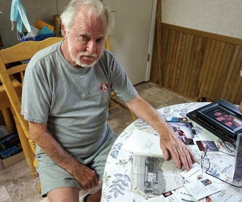 John Perdzock, a member of St. Joseph Church in Conway, sits amid family photos and funeral cards with a newspaper clipping about his stepdaughter Gayle Reynolds and her husband Jeff's deaths June 20, 2020. Jeff Reynolds shot his wife, dog and then himself.