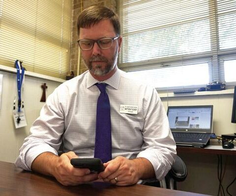 Matt Tucker, lead and high school principal at St. Joseph School in Conway, looks at his phone while his computer screen displays a parent Facebook group for the school community Aug. 12. Tucker said he has seen an uptick in the negative tone used online toward teachers.