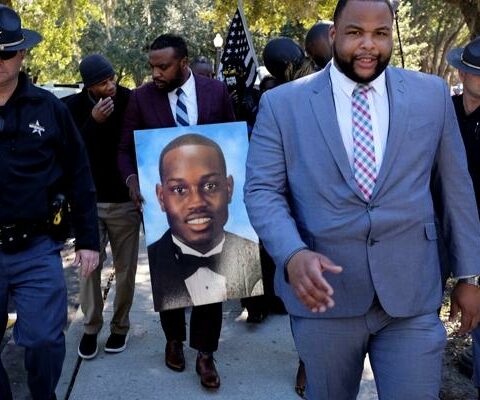 Attorney Lee Merritt holds a poster depicting Ahmaud Arbery as he leaves the Glynn County Courthouse in Brunswick, Ga., Nov. 23, 2021. The following day, the jury found Greg McMichael, his son, Travis McMichael, and William "Roddie" Bryan Jr. guilty of the 2020 murder of the 25-year-old.