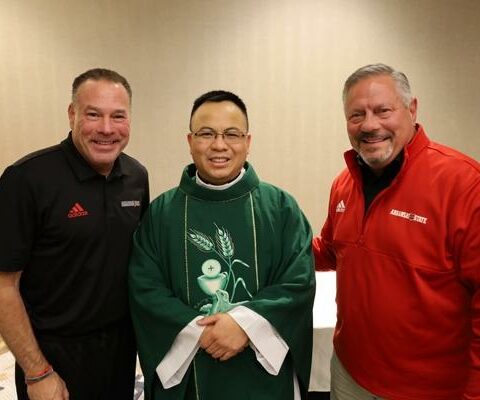 Arkansas State Head Football Coach Butch Jones (left) and Tom Bown, ASU vice chancellor of intercollegiate athletics, share a moment after Mass with Father Tuyen Do Nov. 26.