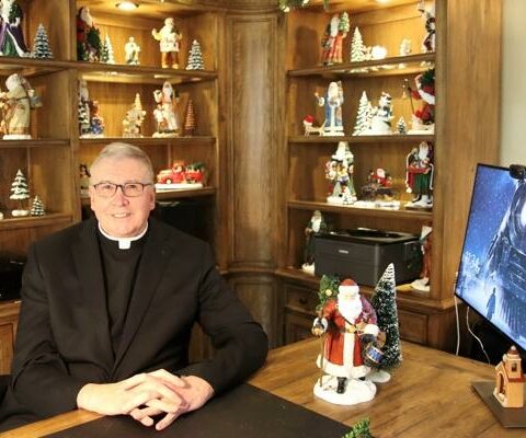 Father John Connell sits in his office decorated for Christmas Dec. 7. An auction of many of his items from his extensive Christmas collection will be auctioned off in July to benefit St. Raphael Parish in Springdale.
