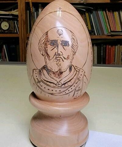 Liturgical artist George Hoelzeman crafted this wooden egg, photographed Feb. 4 in his home library/drafting room, with the image of St. Pope Callistus I. The customizable eggs are available for order.