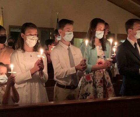 The Plummer family held lit candles during Easter Vigil April 3, 2021, the night they came into the Church at St. Jude Thaddeus in Waldron. Pictured are children Edie (left), Evilee and Josiah, along with parents Evanie and Trey Plummer.