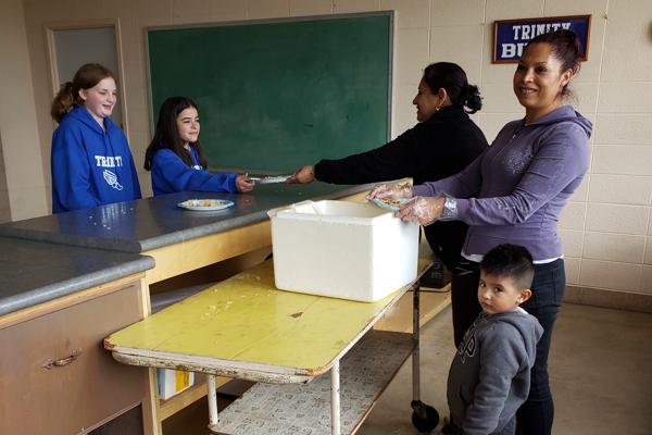 Trinity seventh-graders Ava Edwards (left) and Karlee Rusin get pupusas for lunch at Trinity Catholic School, prepared by volunteers Agueda Guerrero and Angie Manjarrez, accompanied by 3-year-old Andrew Manjarrez, April 10.