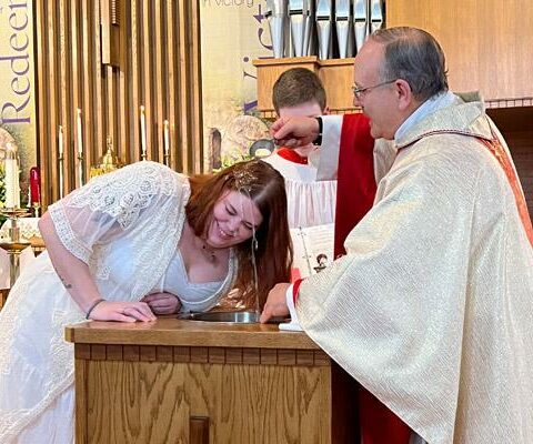Pastor Father Norbert Rappold baptizes Emily Beyer as she joins the Church during Easter Vigil Mass at St. Peter the Fisherman Church in Mountain Home April 8. He is assisted by altar server Francis Kelly.