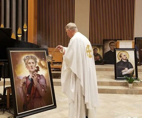 Msgr. David LeSieur, pastor of St. Vincent de Paul Church in Rogers, blesses a portrait of St. Cecilia and other saints during the All Saints Day Mass Nov. 1. The 14 framed portraits will be placed in the meeting rooms that bear their name.