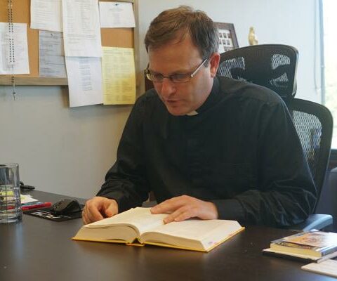 Father Taryn Whittington, associate pastor of St. Joseph Church in Conway and an instructor at the House of Formation in Little Rock, reads about the purpose of work from the Catechism of the Catholic Church in his office at the Spiritan Center in Conway April 11. (Aprille Hanson Spivey)