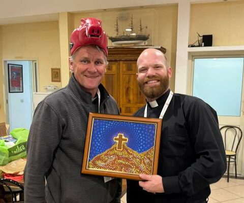 Father Joseph Friend (right) shares his Razorback hat with Father Paul Crotty of Australia, who brought a painting from the indigenous people of his country.