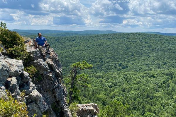 Father Ruben Quinteros, pastor of Immaculate Heart of Mary Church in North Little Rock (Marche) and St. Mary Church in North Little Rock, sits on the side of a rock face on Flat-Side Pinnacle in Perryville August 2022. (Courtesy Father Ruben Quinteros)