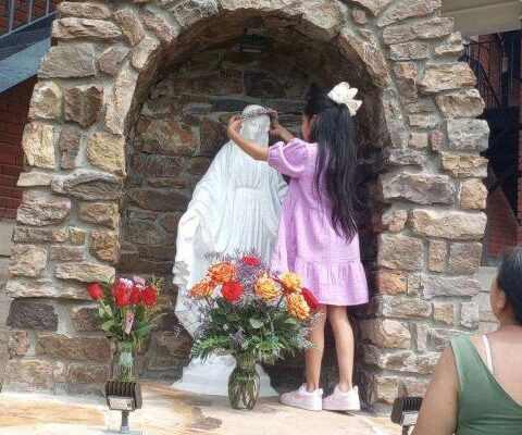 Mayra Palma watches as her second-grade daughter Alice places a crown of flowers on the statue of Mary in the new grotto at St. Boniface Church in Fort Smith May 12. (Kristyn Holden)